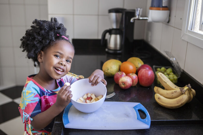 A little girl eating a bowl of fruit.